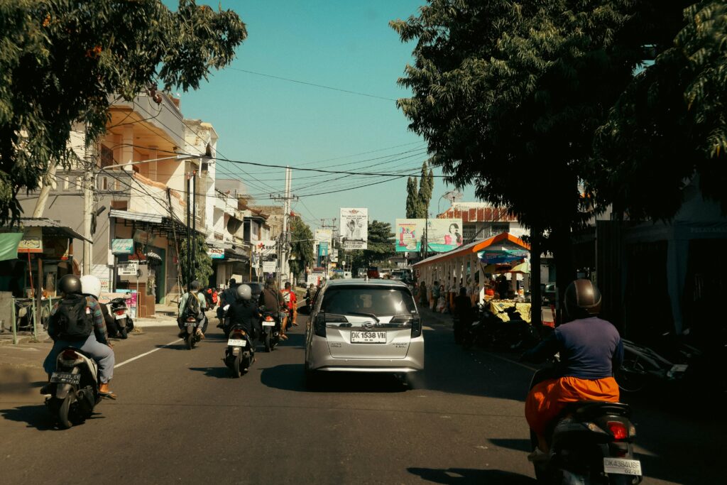 Busy urban road in Bali, Indonesia with motorcycles and cars under a sunny sky.