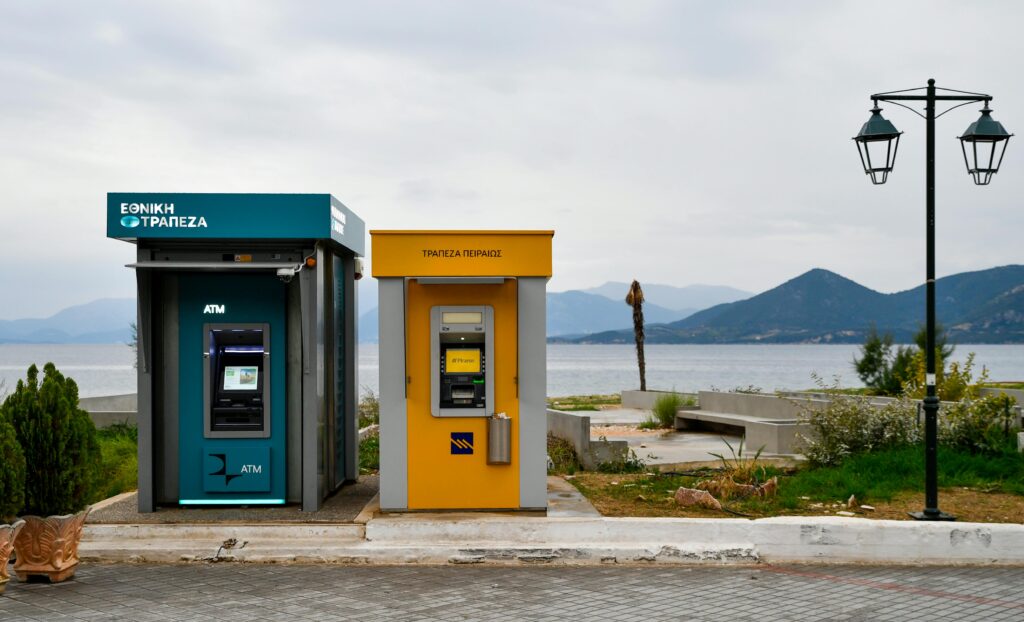 Outdoor ATMs by the Aegean coast in Greece with a scenic view of mountains and sea.