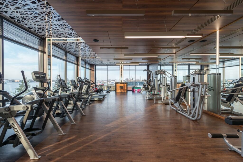 Interior of modern spacious fitness club with various sports machines and equipment placed on parquet floor near panoramic windows
